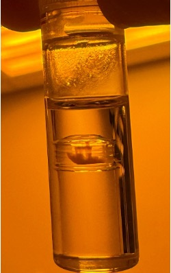 A glass vial of amber resin held up to the light, a cured plug of polymer suspended in the liquid